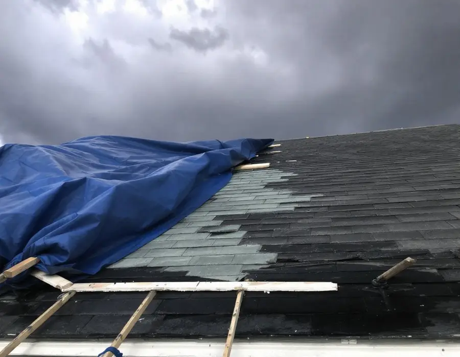 Tarp battened down over storm-damaged shingles under a clearing sky
