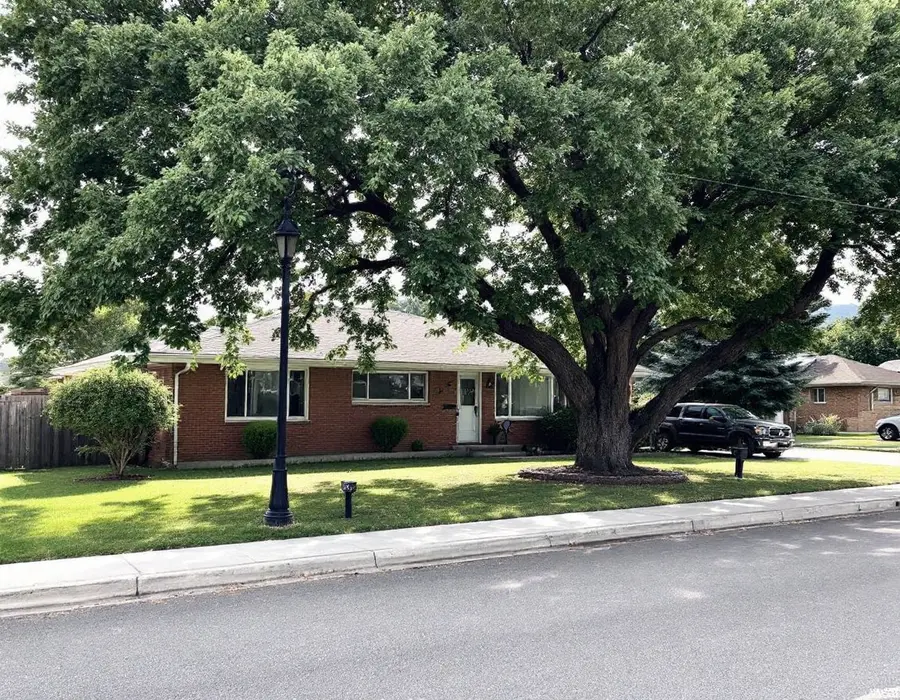 Mid-century brick home under mature shade trees on a Kaysville street