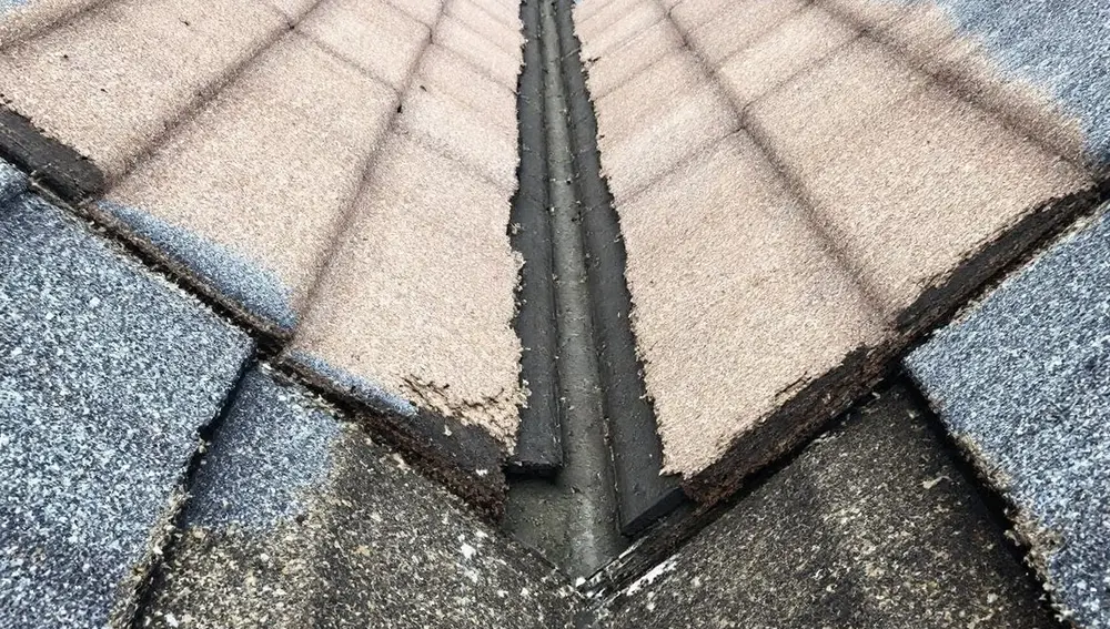 Worn roof valley with shingles torn away to the underlayment and flashing