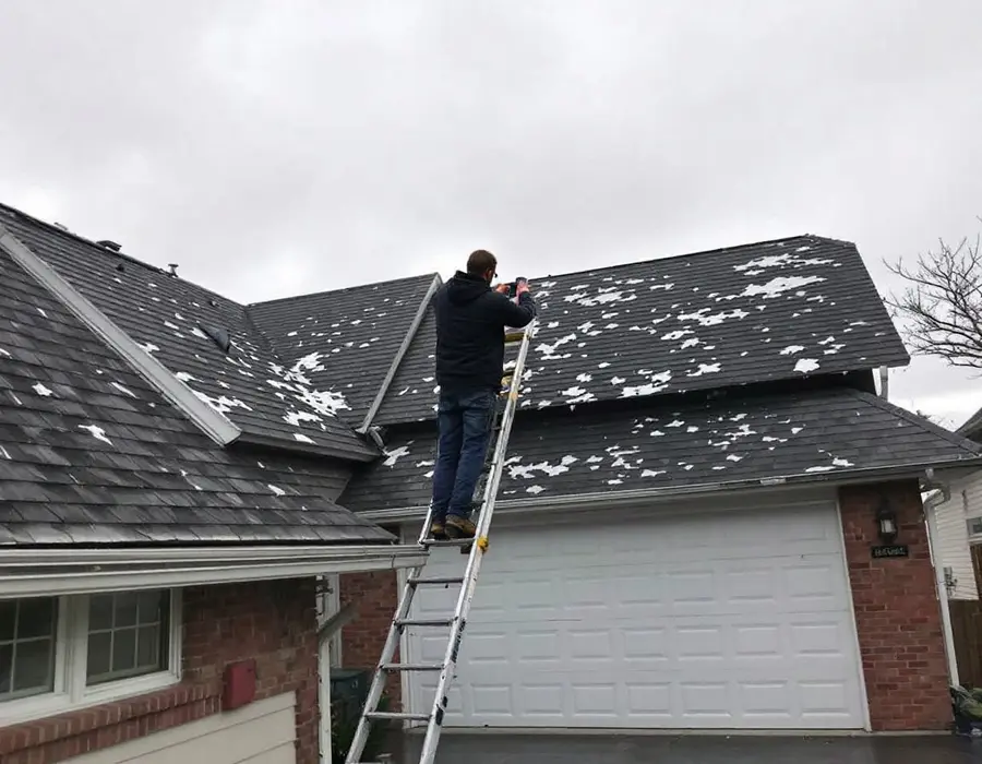 Roofer on a ladder at the eave photographing hail damage after a storm