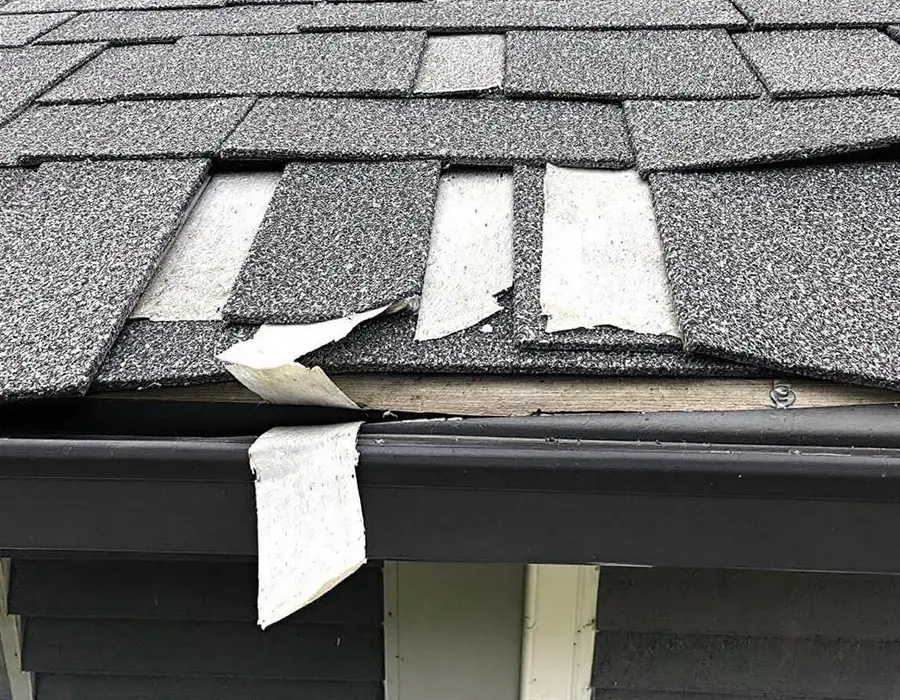Shingle tabs peeled up along the eave after a windstorm, one missing