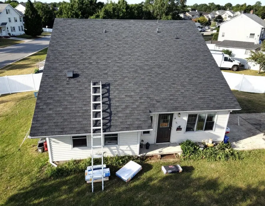 Subdivision home with a brand-new shingle roof, ladder at the eave and bundles on the lawn
